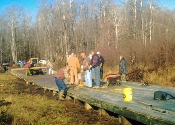 Manpower from two clubs complete a 300-foot bridge east of Minong WI, October 2009. The bridge allows ATV's to use a snowmobile trail that crosses a wetland. The deck is wavy, because you can't do any digging or filling in a wetland to level it out. If you are wondering why a bridge is being built across what looks like a grassy field, see previous picture.