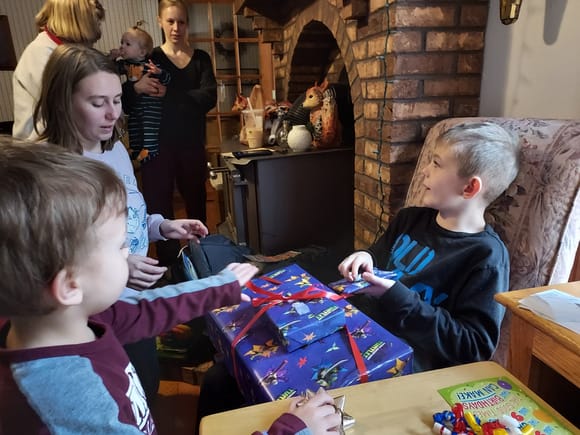 Gabe opening presents with Mom, brother Keegan in the foreground.   My oldest daughter Taylor is in the background holding our granddaughter Anna.