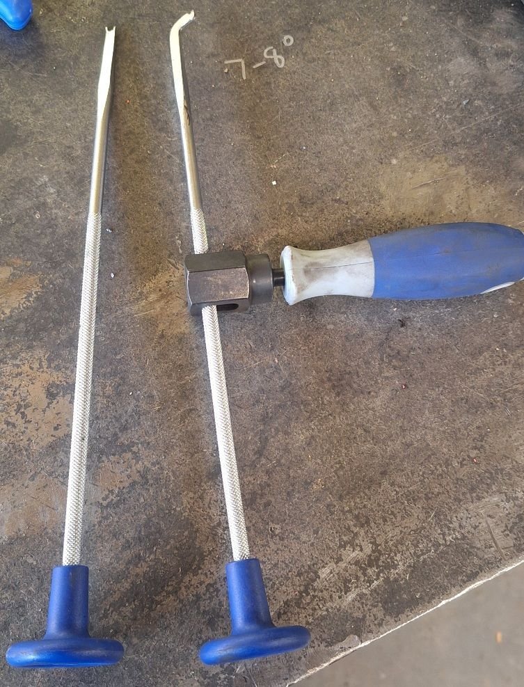 The forked ends may catch the wrapped spring nicely to force it toward the backing plate to hook the bent nail?  The handle can be set anywhere along the length of the shaft