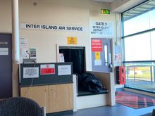 Gate 3 of Kirkwall Airport. This gate is within the main concourse, meaning no security checks at all. Next to it are seats with television showing BBC News (as usual)