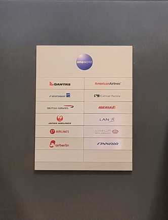 Went up to the Departures level to the QF sales desk to explore options. While I was waiting to be served, I noticed the out-of-date OneWorld alliance member board!

The lady at the desk did seem to make as many attempts to put me on a different flight, but advised I call AA regarding my itinerary. After 24 min on hold, I spoke with an agent at AA, and they, somewhat predictably, pushed me back to the QF sales desk. Sadly, no options could be explored, so into town I went to hang out with mates.