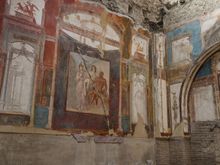 The Hall of the Sacelli Augustals. In this mural, we see Hercules in Olympus with Juno and Minerva. Freedmen had once adorned this building, while maintaining their cult of worshipping the Emperor Augustus as a God. As elsewhere, today lava foam scars and cracks are present throughout. 