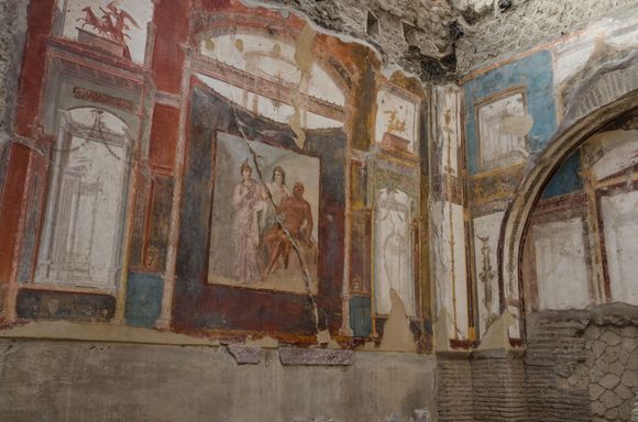 The Hall of the Sacelli Augustals. In this mural, we see Hercules in Olympus with Juno and Minerva. Freedmen had once adorned this building, while maintaining their cult of worshipping the Emperor Augustus as a God. As elsewhere, today lava foam scars and cracks are present throughout. 