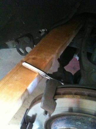 Applying pressure with 2x4 to loosen bolt for rotor removal.