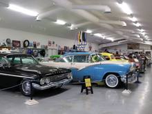 Small museum two rows of cars, other items of interest around the museum and on walls
