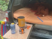 The idea of placing the hatch covers on top of the drawers to create a table ended up working really well. Here's us using the drawer as a table to boil some water under the tailgate and mostly out of the rain.